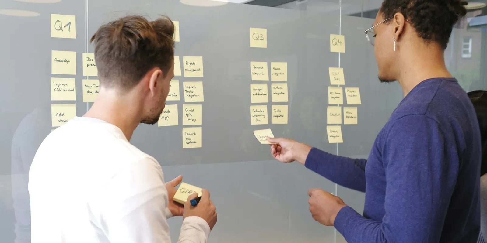 Two colleagues breaking a quarterly plan into tasks on a glass wall